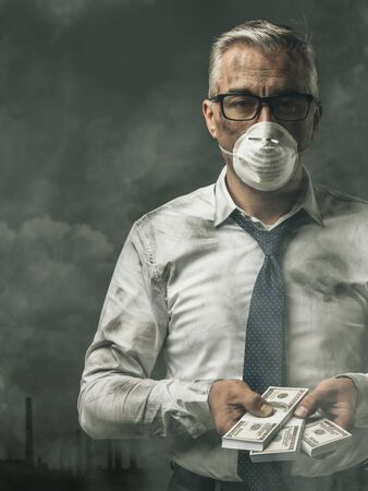 Greedy business executive wearing a mask and holding cash banknotes: pollution and corruption conceptの写真素材