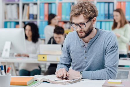 University student sitting at desk and using a digital tablet, group of students in the background