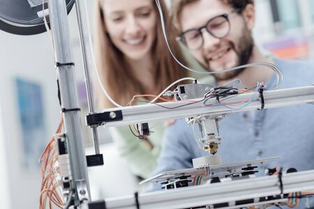Smiling students using a 3D printer in the school laboratory, they are printing prototypes, technology and learning conceptの写真素材