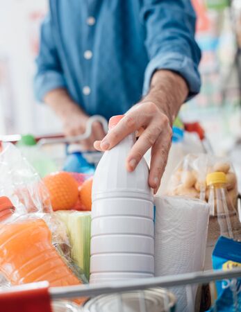 Man doing grocery shopping at the supermarket, he is putting a bottle of milk in the cartの写真素材