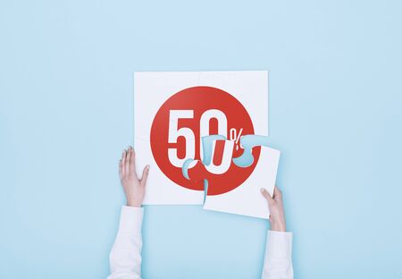 Woman completing a puzzle with a 50% off discount icon, she is putting the missing piece, shopping and discounts conceptの写真素材