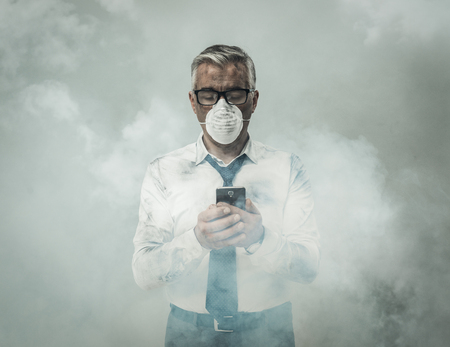 Corporate business executive with protective mask and smog, he is using a smartphoneの写真素材