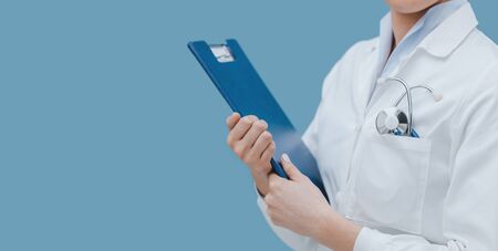 Professional female doctor holding a clipboard and posing, healthcare professionals conceptの写真素材