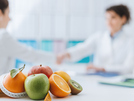 Professional nutritionist meeting a patient in the office and healthy fruits with tape measure on the foreground: healthy eating and diet conceptの写真素材