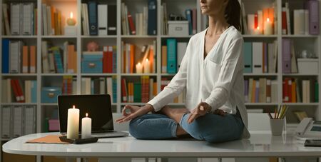 Relaxed woman practicing meditation at home at night, she is sitting in the lotus position on the...