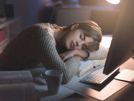 Tired young woman sleeping on the office desk late at night, overtime work and deadlines concept