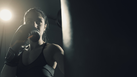 Young woman doing boxing training at the gym, she is wearing boxing gloves and hitting the punching bagの写真素材