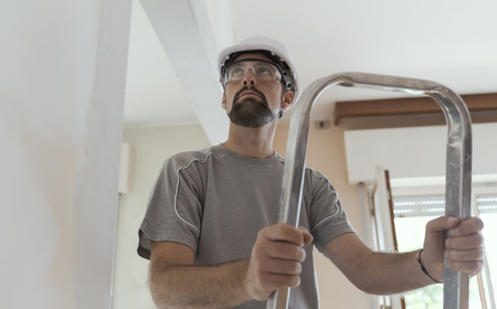 Professional construction worker doing a home makeover, he is standing on a ladder and looking...