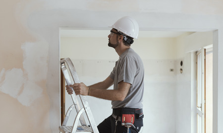 Professional construction worker doing a home makeover, he is standing on a ladder and looking...
