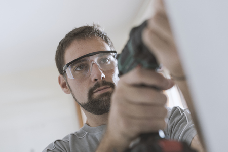 Professional repairman with protective goggles, he is using a drill and doing a home renovation