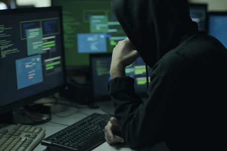Young hacker with a hoodie thinking with hand on chin and working with computers, technology and...