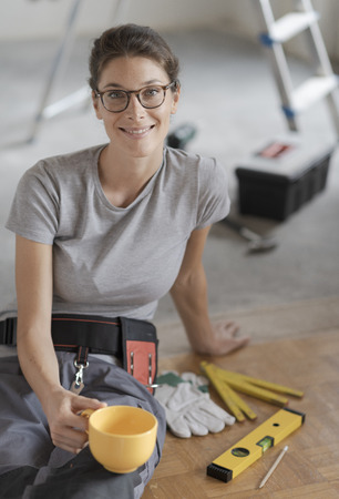 Young smiling woman having a coffee break and sitting on the floor, she is doing a home renovationの写真素材