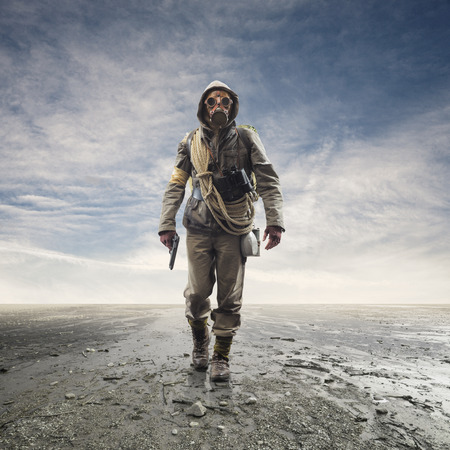 Brave soldier with gas mask and gun walking in a polluted post atomic landscape with toxic smog and...