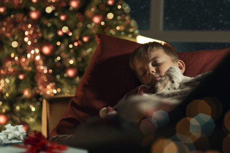 Cute boy sleeping in the living room next to the Christmas tree and waiting for Santa on Christmas Eveの写真素材