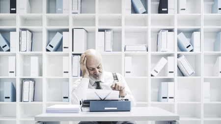 Senior lazy businessman or journalist working in the office, he is sitting at desk and using a...