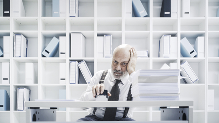 Senior corporate clerk doing a boring job in the office, he is stamping paperworkの写真素材