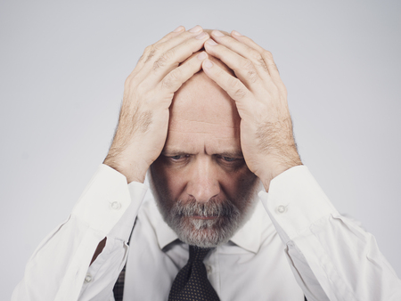 Desperate mature man with head in hands: he is feeling depressed, exhausted and hopeless
