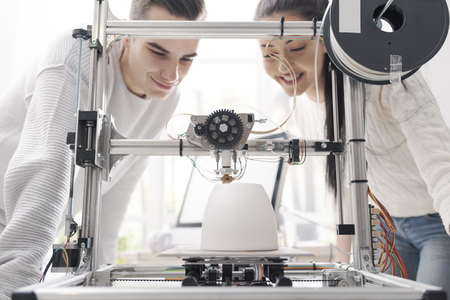 Engineering students using an innovative 3D printer in the university lab, they are printing a...