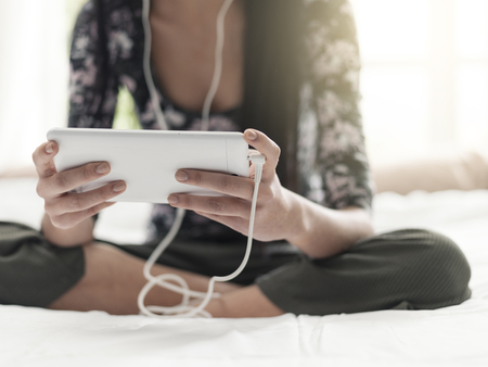 Girl relaxing in her bedroom, she is sitting on the bed, watching videos and listening to music...