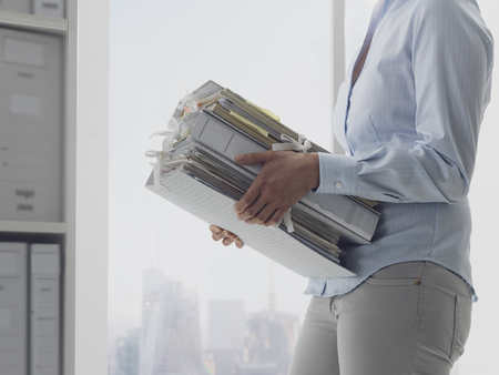Female office worker carrying folders and files in the archive, administration and business conceptの写真素材
