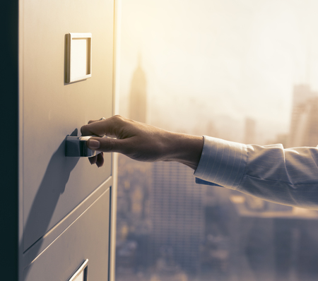 Professional secretary working and searching files in the archive, she is opening a filing cabinet's...