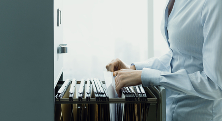 Professional female office clerk searching files and paperwork in the filing cabinetの写真素材