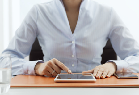 Female office worker sitting at desk and working with a digital touch screen tabletの写真素材