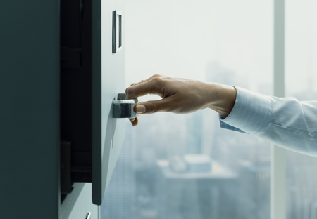 Professional secretary working and searching files in the archive, she is opening a filing cabinet's drawerの写真素材