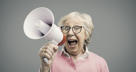 Cheerful senior woman shouting into a megaphone, communication and advertising conceptの写真素材