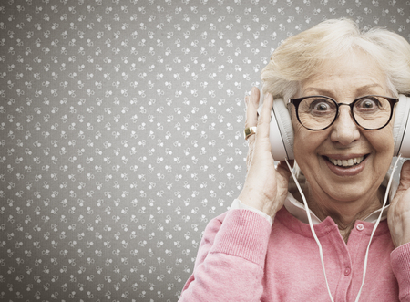 Happy senior woman wearing headphones and listening to some good music, she is cheerful and enjoying
