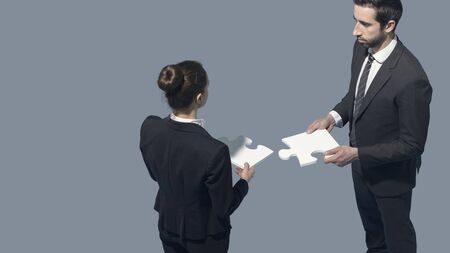 Business people assembling a jigsaw puzzle: cooperation, teamwork and skills concept, blank copy spaceの写真素材