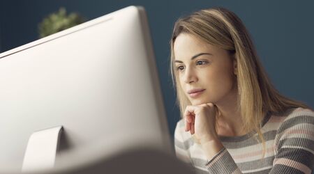 Young attractive woman sitting at desk and working with her computer, she is smiling and looking at...