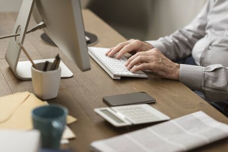 Senior retired man sitting ad desk and working with a computer, elderly and technology concept,...