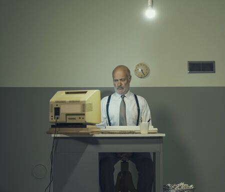 Sad senior businessman working with an outdated computer on a small desk, he is sad and disappointedの写真素材