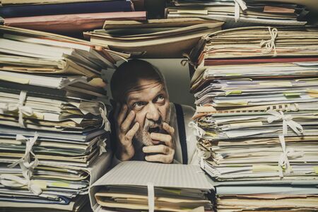 Panicked stressed businessman overwhelmed with paperwork, taxes and accounting concept