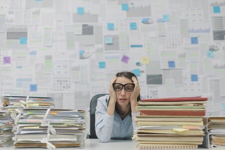 Stressed businesswoman with head in hands, she is sitting at office desk and she is overloaded with...