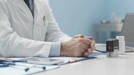 Doctor sitting at desk in the office and waiting for a patient, hands close up, medicine and...
