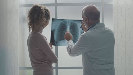Professional senior doctor checking a patient's radiography at the clinic, the woman is listening to...