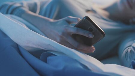 Female patient lying in bed at the hospital and chatting with her smartphone at nightの写真素材