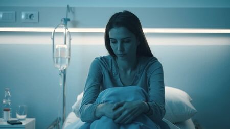 Sad female patient lying in the hospital bed at night, she is sleepless, lonely and worriedの写真素材