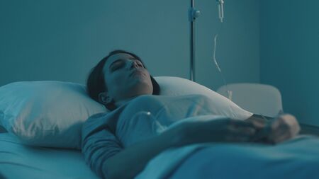 Young woman lying in a hospital bed at night and sleeping with IV dripの写真素材