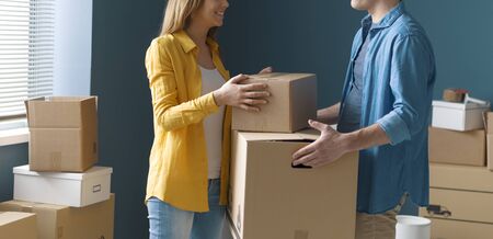 Happy couple moving in their new house: the man is carrying a box and his girlfriend is helping him