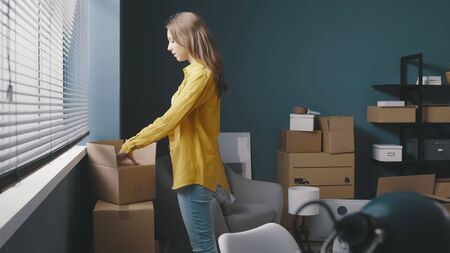 Woman moving in a new house, she is unboxing and searching in cardboard boxes