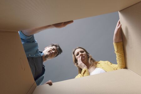 Happy couple opening a cardboard box and looking inside, they are disappointed and sad