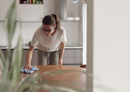 Woman doing housework and cleaning the kitchen table with a cloth, household and hygiene concept