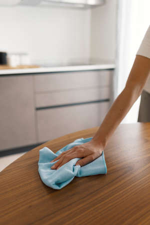 Woman doing housework and cleaning the kitchen table with a cloth, household and hygiene concept
