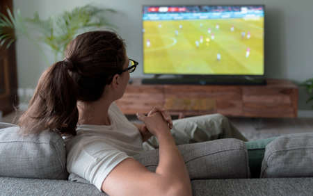 Woman relaxing on the couch at home and watching football on TVの写真素材