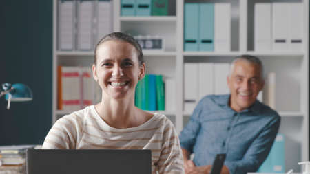 Business people posing in the office, they are sitting at desk and smiling at cameraの写真素材