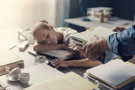 Tired lazy woman sleeping on the office desk, her boss is bringing a pile of paperwork to her desk