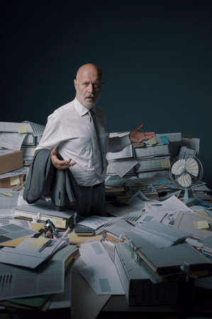 Disappointed stressed businessman standing in his office surrounded by lots of paperworkの写真素材